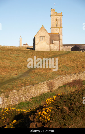 St. Helena Kirche mit alten Leuchtturm Leuchtturm in der Ferne gebadet im Morgenlicht auf Lundy Island, Devon, England UK im März Stockfoto