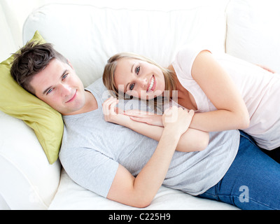 Junges Paar Lyingo zusammen auf dem Sofa im Wohnzimmer zu streicheln Stockfoto