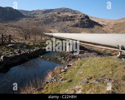 Eine Pipeline, die Zuführung von Wasser zu einem hydroelektrischen Kraftwerk kreuzt die Afon Glaslyn in Cwm Dyli unter dem Gipfel des Snowdon. Stockfoto