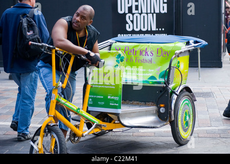 Schwarze jungen Mann durch seine pedal Rikscha in Ad für St Patrick's Day Festival & Parade decked warten Stockfoto