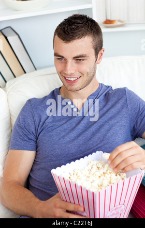 Lachend kaukasischen Mann isst Popcorn auf dem sofa Stockfoto