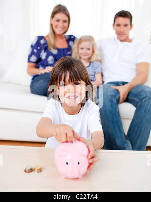 Fröhliche kleine Junge einfügen Münze in ein Sparschwein Stockfoto