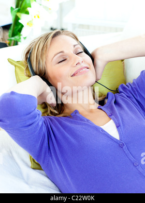Entspannte kaukasischen Frau Musikhören mit Kopfhörer auf einem Sofa liegend Stockfoto