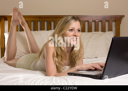 Attraktive junge, blonde Frau Handauflegen Magen auf Bett während der Eingabe auf Laptop-computer Stockfoto