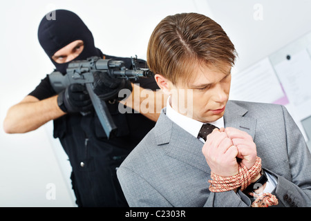 Porträt von verwirrt Geschäftsmann mit gefesselten Händen gejagt von Gangster zeigenden Waffe auf ihn Stockfoto