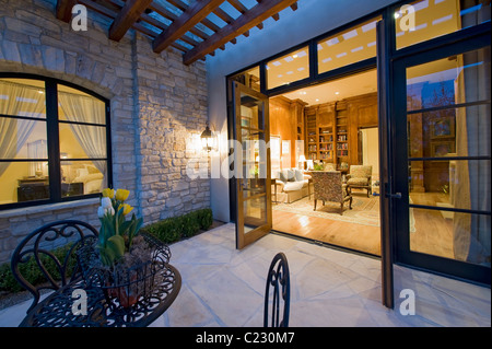 Haus außen in der Nacht mit einigen Patio-Möbel und offenen Terrassentüren, die auf der Suche in den beleuchteten Innenraum Stockfoto