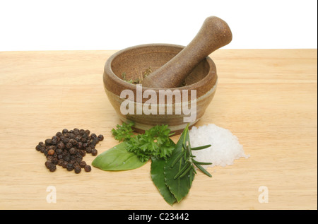 Frische Kräuter, Salz, Pfefferkörner mit einem Stößel und Mörser auf einem Holzbrett Stockfoto