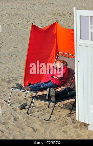 Touristen, die hinter der Windschutz am Strand Sonnenbaden, im frühen Frühling, Ostende, Belgien Stockfoto