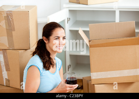 Lächelnde Frau Weintrinken zwischen Leerboxen Stockfoto