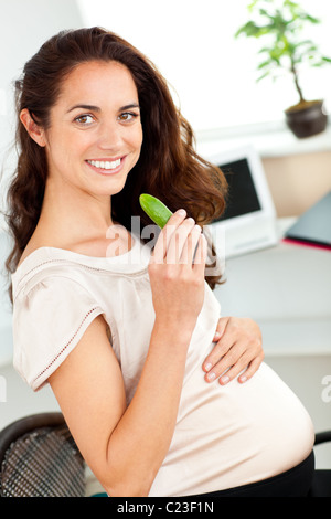 Hellen schwangere Essen eine Gurke in ihr Büro Stockfoto