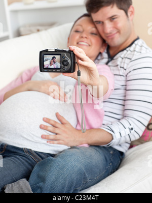 Eine freudige schwangere Frau und ihr Mann die Bilder von sich selbst auf einem Sofa in Nahaufnahme Stockfoto