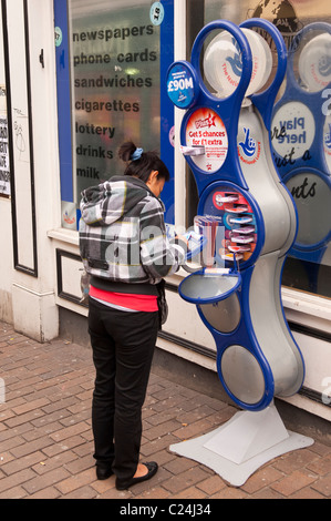 Eine Frau, füllen Sie ihre Lottoscheine vor einem Geschäft in Norwich, Norfolk, England, Großbritannien, Uk Stockfoto