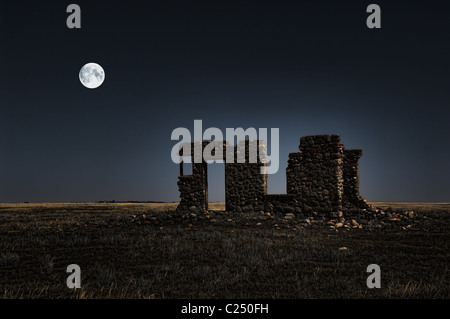 Ein surrealistisches Bild der Ruinen von einem alten Bauernhaus in der Nacht mit dem Mond im Hintergrund. Stockfoto