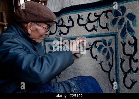 Eine ältere resident trimmen und finishing Teppiche an den tibetischen Flüchtlingen Selbsthilfe Zentrum in Darjeeling, Westbengalen, Indien. Stockfoto