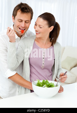 Hübsche Frau, die eine Tomate zu seinem Freund während der Vorbereitung eines Salats geben Stockfoto