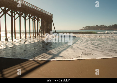 Hölzerne Pier wirft einen Schatten auf schäumenden Wellen gegen den Strand bei Ebbe in San Simeon an der zentralen Küste Kaliforniens Stockfoto