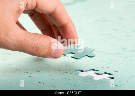 Hand, die fehlendes Stück Grün Puzzles in das Loch einsetzen Stockfoto