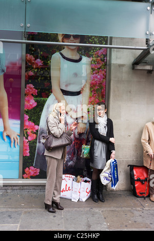 Frauen-Shopping-Süchtige ruhen während Einkaufsbummel außerhalb ein Zweig der Marks & Spencer in der Londoner Innenstadt. Stockfoto