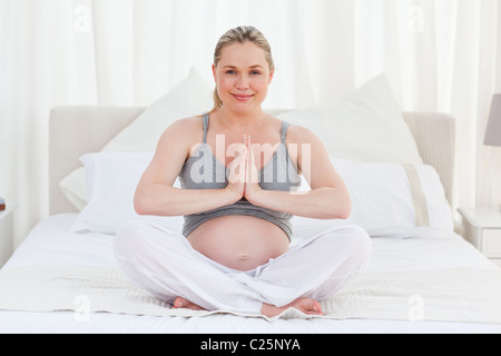 Schwangere Frau praktizieren Yoga auf ihrem Bett Stockfoto