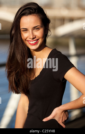 Porträt einer jungen Frau, lächelnd mit einem Arm auf der Hüfte, London, England, Großbritannien. Stockfoto