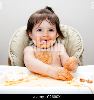 Glückliches Baby Spaß Essen chaotisch bedeckt in Angel Hair Pasta Spaghetti rot marinara Tomatensauce. Stockfoto