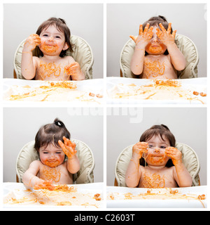 Glückliches Baby Spaß Essen chaotisch zeigt Hände in Angel Hair Pasta Spaghetti rot marinara Tomatensauce bedeckt. Stockfoto