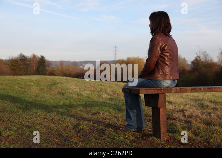 Rückansicht einer Frau tief in Gedanken mit Blick auf einen See, auf einer Parkbank sitzen. Stockfoto