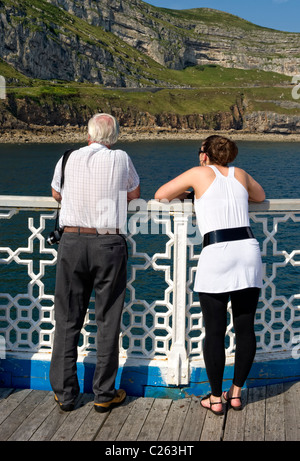 Mann und Frau auf der Schiene von Llandudno Pier gelehnt und mit Blick auf den Great Orme Stockfoto
