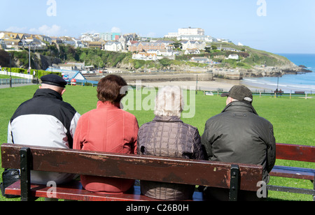 Vier Leute sitzen auf einer Bank mit Blick auf die Küste bei Newquay in Cornwall, Großbritannien Stockfoto