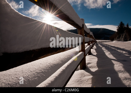 Die Sonne shinning durch ein Schnee bedeckt Holzzaun Stockfoto