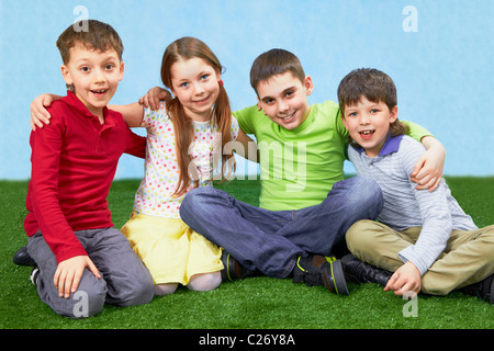 Gruppe von vier Kinder sitzen auf einem grünen Rasen Stockfoto