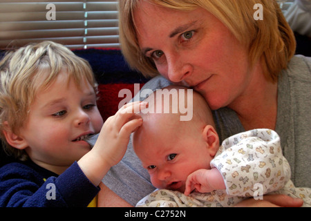 Ein vier Jahre alter Junge, der seinen Neugeborenen Bruder, als seine Mutter kennenlernen blickt auf. Stockfoto