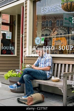 Ein junger Mann liest auf einer Bank vor einem Café in Boston. Stockfoto