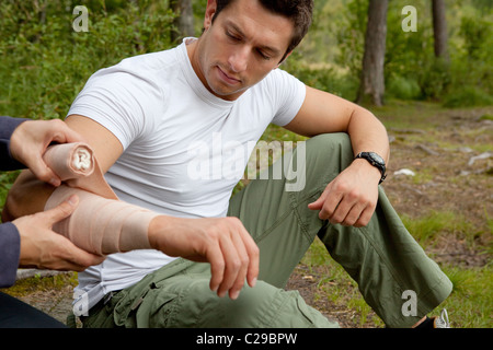 Eine Frau, eine Arm-Bandage auf einen männlichen Camper - Fokus auf männliche Gesicht auftragen Stockfoto