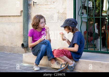 Zwei Kinder genießen ihre Eis sitzen auf einige Shop Schritte in Uzes, Gard, Languedoc-Roussillon, Frankreich. Stockfoto