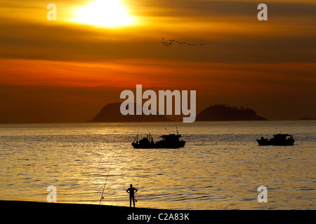 Fischer in Barra da Tijuca Strand bei Sonnenaufgang mit Fischerbooten im Hintergrund. Stockfoto