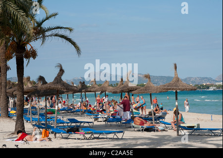 Urlauber, die zum Sonnenbaden unter Palmen am Strand im schönen Spanisch Resort Puerto de Alcudia Stockfoto