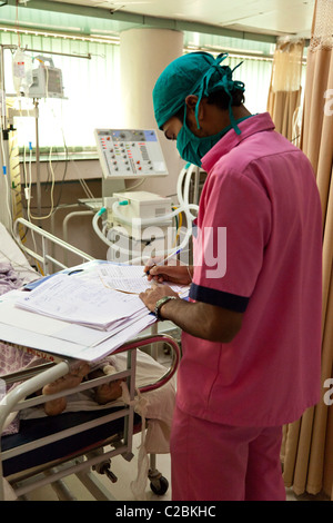 Eine Krankenschwester prüft eine Patienten-Noten in eine Intensive Care Unit (ICU) in Indien Yashodhara Krankenhaus Sholapur Stockfoto