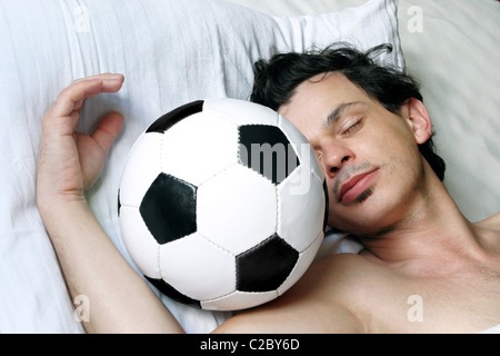 Ein Mann liegt im Bett mit einem Fußball Stockfoto