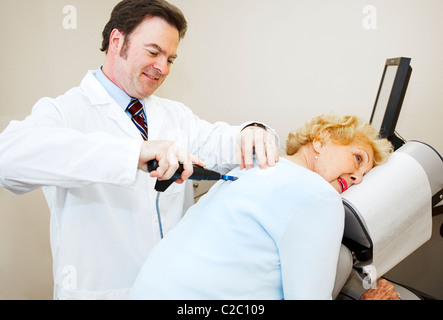 Freundlich, lächelnd Chiropraktiker Anpassung eine ältere Frau zurück. Stockfoto