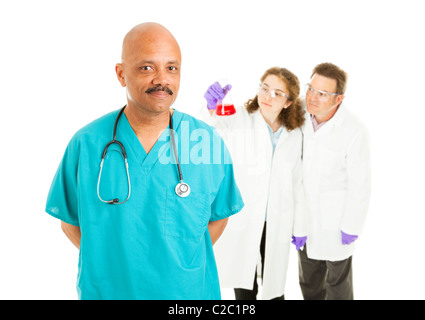Gut aussehend afrikanisch-amerikanischer Chirurg mit Labor-Techniker im Hintergrund. Isoliert auf weiss. Stockfoto