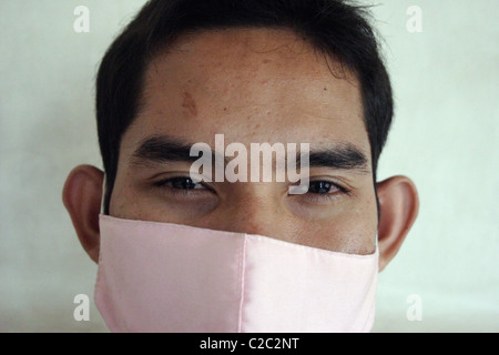 Ein junger asiatischer Mann trägt einen Mundschutz um sich vor giftigen Reinigungsmitteln zu schützen, mit denen er, in einem Hotel in Kambodscha zusammenarbeitet. Stockfoto