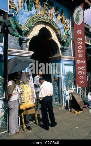 Mann, der Lottoscheine verkauft und Bettler unter dem Schirm beim Eingang, Kataragama Devalaya Tempel, Kandy, Central Province, Sri Lanka Stockfoto