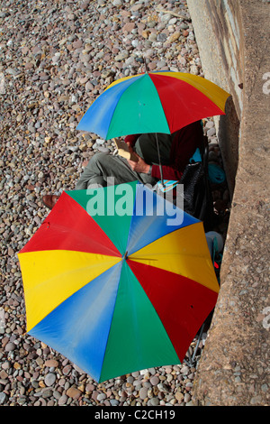 Englisches Paar sitzen an einem Strand in Devon mit bunten Sonnenschirme Stockfoto