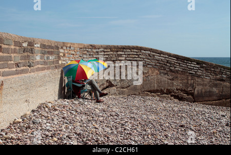 Englisches Paar sitzen an einem Strand in Devon mit bunten Sonnenschirme Stockfoto