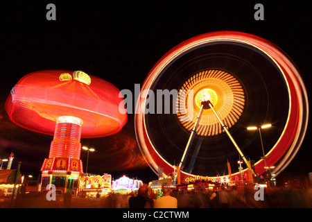 Ein Karussell dreht sich durch das große Rad in der Nacht auf dem Münchner Oktoberfest in Deutschland. Stockfoto