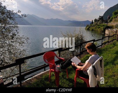 Frau sitzt und liest am Lago d Iseo in Riva di Solto, Bergamo, Italien Stockfoto