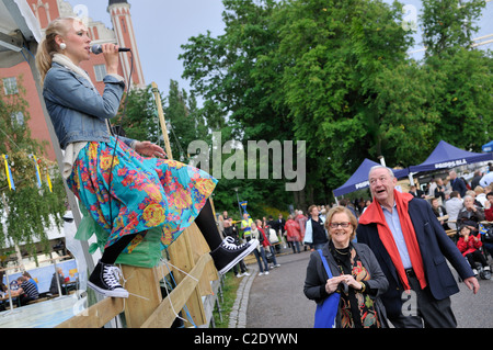 Jüngere Frau singt beim Sitzen auf einem hölzernen Zaun in Stockholm, Stockholms Lan, Schweden Stockfoto