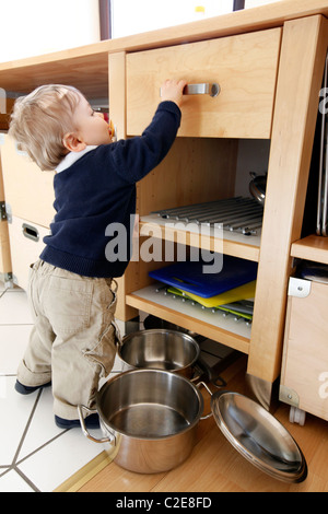 Kleiner Junge, Baby, 10 Monate alt, ist die Erkundung der Küche, spielt mit Kochtöpfen. entfernt die Töpfe aus Küchenschrank. Stockfoto