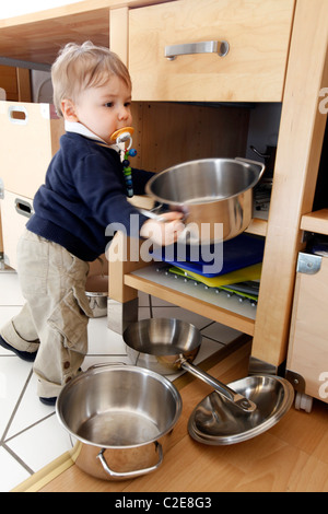 Kleiner Junge, Baby, 10 Monate alt, ist die Erkundung der Küche, spielt mit Kochtöpfen. entfernt die Töpfe aus Küchenschrank. Stockfoto